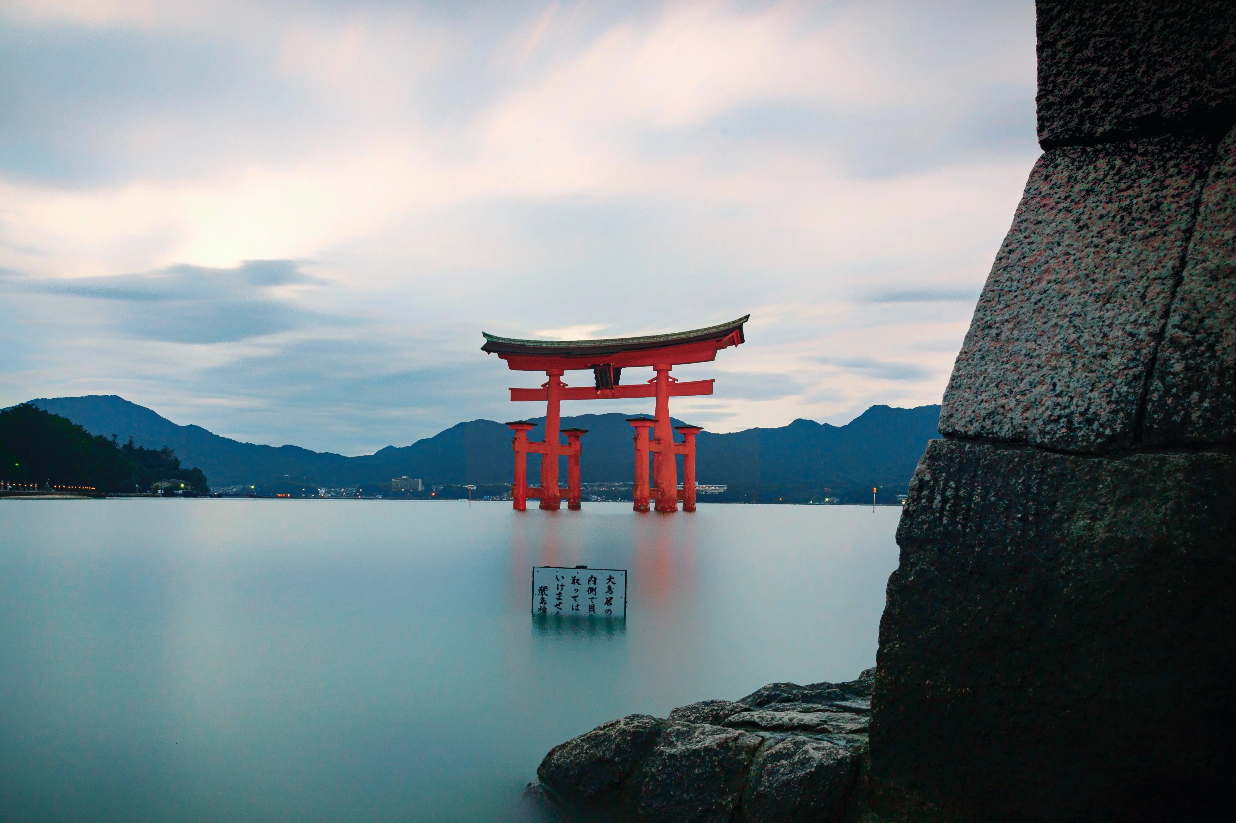 Photo of red Japanese torii gate sticking out of water infront of mountains at dusk